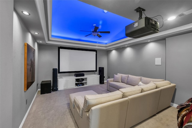 home theater room featuring light carpet, ceiling fan, and a tray ceiling