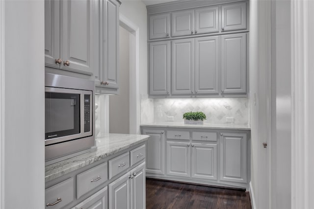 kitchen featuring dark wood-type flooring, stainless steel microwave, light stone countertops, and decorative backsplash