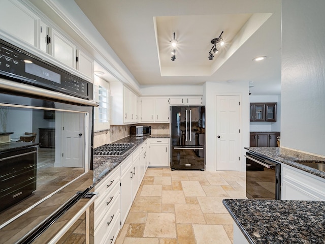 kitchen with a raised ceiling, white cabinetry, dark stone counters, and black appliances