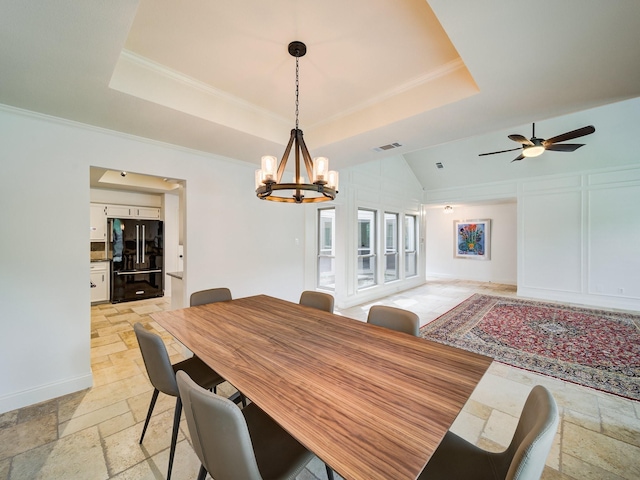 dining space with a raised ceiling, ceiling fan with notable chandelier, and ornamental molding