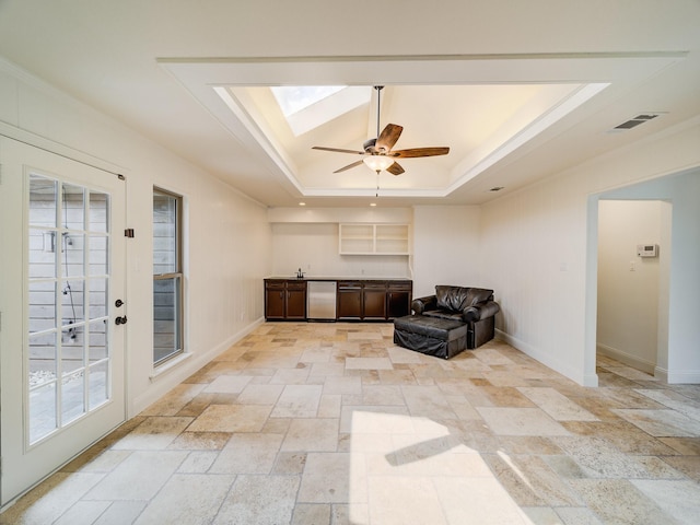 sitting room with a skylight, a tray ceiling, plenty of natural light, and ceiling fan