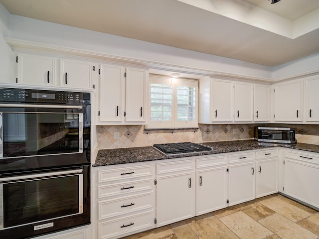 kitchen with backsplash, stainless steel appliances, white cabinetry, and dark stone countertops