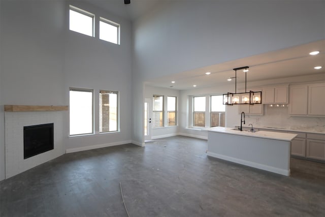 unfurnished living room with recessed lighting, a fireplace, a sink, a towering ceiling, and baseboards