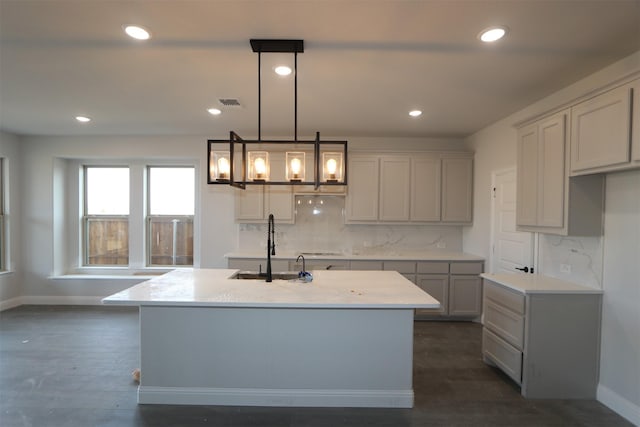 kitchen with a kitchen island with sink, gray cabinetry, visible vents, hanging light fixtures, and dark wood finished floors