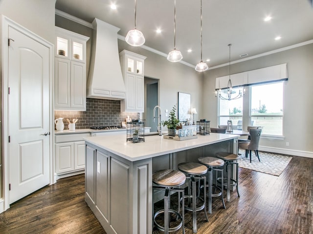 kitchen featuring tasteful backsplash, decorative light fixtures, a center island with sink, white cabinets, and custom range hood