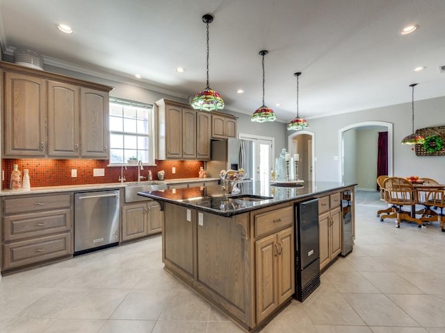 kitchen with dark stone counters, crown molding, appliances with stainless steel finishes, decorative light fixtures, and a kitchen island