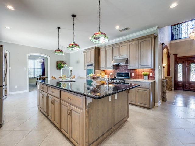 kitchen featuring pendant lighting, a center island with sink, dark stone countertops, ornamental molding, and appliances with stainless steel finishes