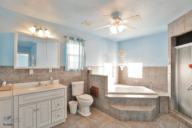 full bathroom featuring ceiling fan, a textured ceiling, toilet, vanity, and tile walls