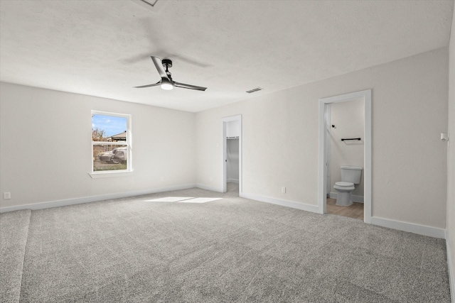 unfurnished bedroom featuring light carpet, ensuite bathroom, a walk in closet, ceiling fan, and a closet