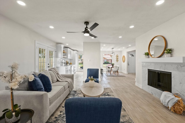 living room with french doors, light wood-type flooring, ceiling fan, sink, and a premium fireplace