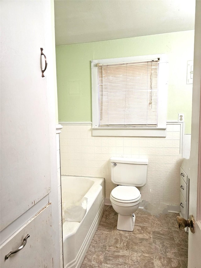 bathroom with a washtub, toilet, and tile walls