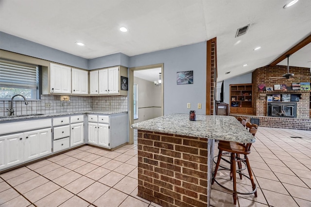 kitchen with a brick fireplace, light stone counters, sink, vaulted ceiling with beams, and white cabinetry