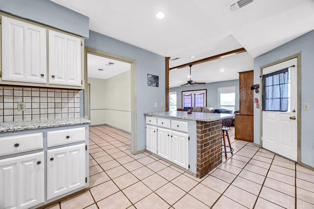 kitchen with light stone countertops, backsplash, a breakfast bar, ceiling fan, and white cabinetry