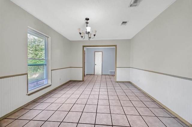 tiled empty room featuring an inviting chandelier