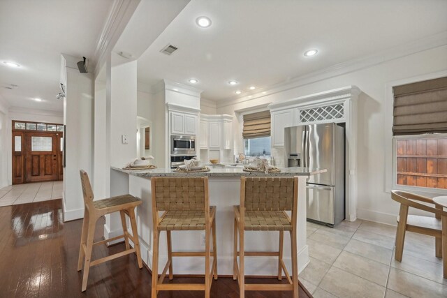 kitchen with kitchen peninsula, light hardwood / wood-style flooring, ornamental molding, appliances with stainless steel finishes, and white cabinetry