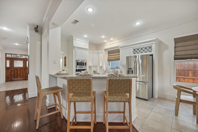 kitchen featuring appliances with stainless steel finishes, white cabinetry, a breakfast bar area, ornamental molding, and kitchen peninsula