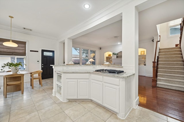 kitchen with crown molding, light wood-type flooring, light stone counters, white cabinetry, and stainless steel gas cooktop