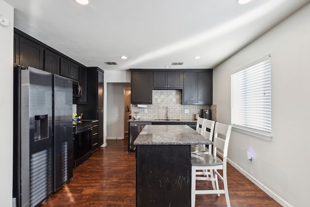 kitchen featuring a kitchen island, appliances with stainless steel finishes, sink, backsplash, and light stone countertops