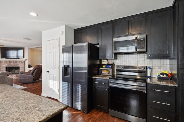 kitchen featuring a brick fireplace, backsplash, stainless steel appliances, and dark hardwood / wood-style floors