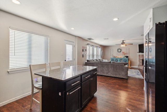 kitchen with light stone countertops, dark hardwood / wood-style floors, a kitchen breakfast bar, and a center island