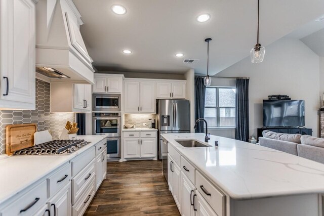 kitchen with appliances with stainless steel finishes, custom range hood, sink, pendant lighting, and white cabinets