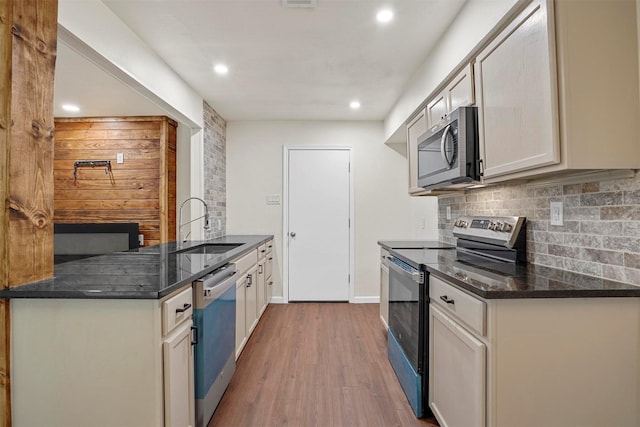 kitchen featuring sink, dark stone countertops, hardwood / wood-style floors, decorative backsplash, and appliances with stainless steel finishes