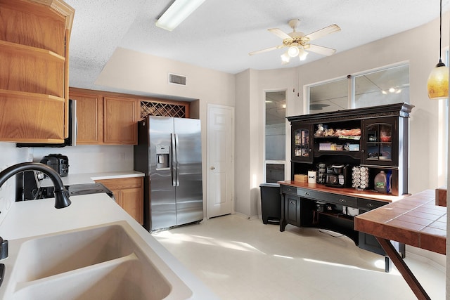 kitchen with a textured ceiling, pendant lighting, stainless steel fridge, ceiling fan, and sink