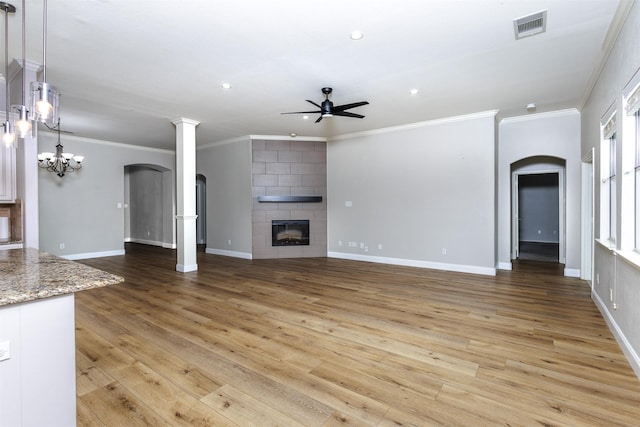 unfurnished living room with a tiled fireplace, crown molding, light hardwood / wood-style flooring, and ceiling fan with notable chandelier