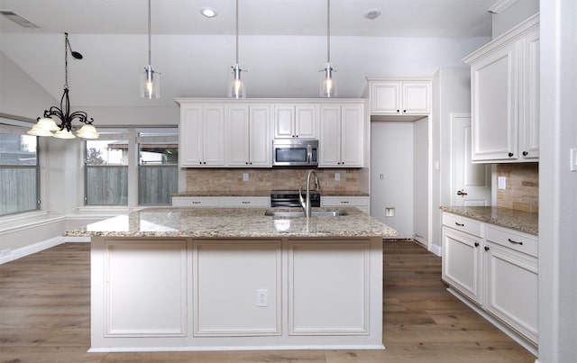 kitchen featuring white cabinetry, a center island with sink, pendant lighting, and light stone counters