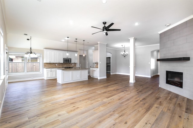 unfurnished living room with a fireplace, ceiling fan with notable chandelier, light hardwood / wood-style flooring, and crown molding