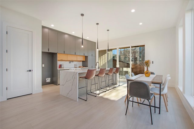 kitchen with gray cabinetry, backsplash, pendant lighting, light hardwood / wood-style floors, and a breakfast bar