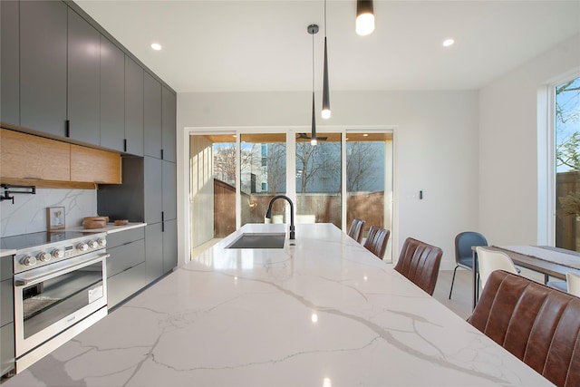 kitchen with decorative backsplash, gray cabinetry, sink, high end stainless steel range, and hanging light fixtures