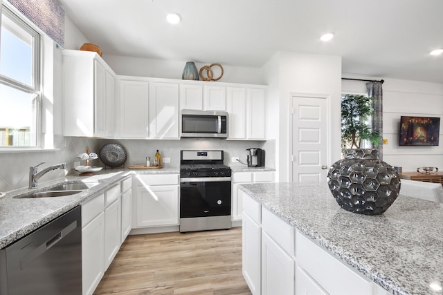 kitchen with light stone countertops, white cabinetry, sink, and stainless steel appliances