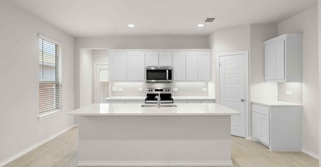 kitchen featuring backsplash, a kitchen island with sink, light hardwood / wood-style floors, white cabinetry, and stainless steel appliances