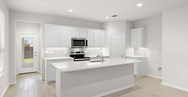 kitchen with a center island with sink, white cabinets, sink, light hardwood / wood-style floors, and stainless steel appliances