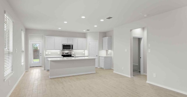 kitchen featuring a kitchen island with sink, white cabinets, light hardwood / wood-style flooring, decorative backsplash, and stainless steel appliances