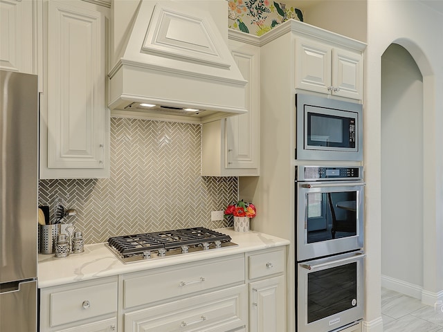 kitchen featuring appliances with stainless steel finishes, tasteful backsplash, white cabinetry, and custom exhaust hood