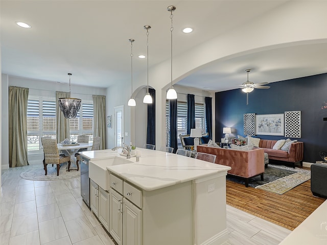 kitchen with light stone countertops, sink, an island with sink, pendant lighting, and ceiling fan with notable chandelier