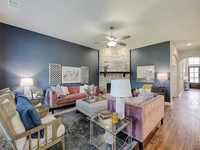 living room featuring dark hardwood / wood-style flooring, a stone fireplace, and ceiling fan