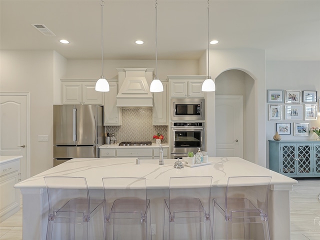 kitchen with light stone counters, pendant lighting, a kitchen bar, a kitchen island with sink, and appliances with stainless steel finishes