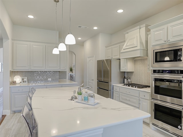 kitchen featuring stainless steel appliances, white cabinetry, hanging light fixtures, and a center island with sink