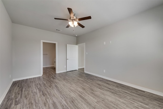 unfurnished bedroom with a spacious closet, a closet, ceiling fan, and hardwood / wood-style flooring