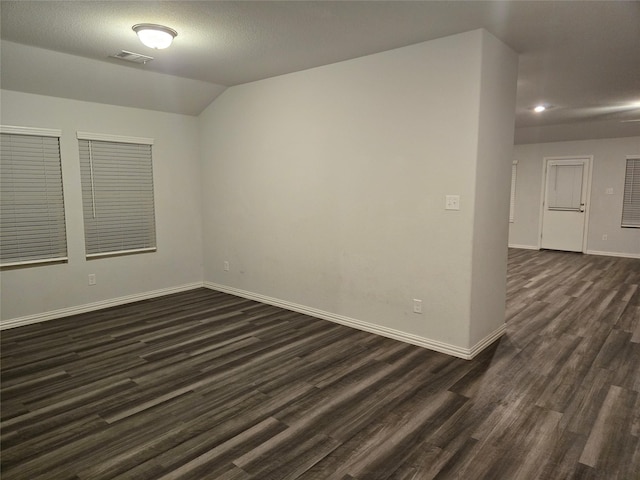 empty room with vaulted ceiling, a textured ceiling, and dark hardwood / wood-style flooring