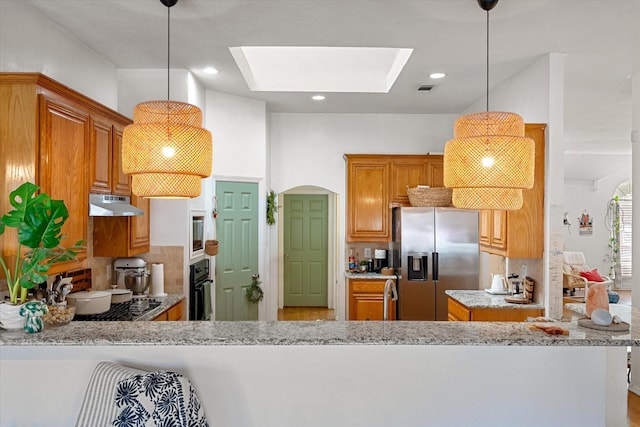 kitchen featuring a skylight, light stone countertops, kitchen peninsula, pendant lighting, and appliances with stainless steel finishes