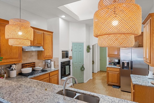 kitchen with appliances with stainless steel finishes, light wood-type flooring, backsplash, sink, and hanging light fixtures