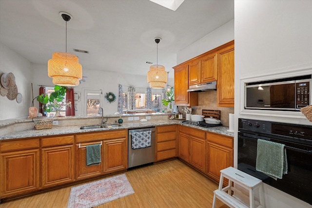 kitchen with light stone countertops, sink, hanging light fixtures, light hardwood / wood-style flooring, and appliances with stainless steel finishes