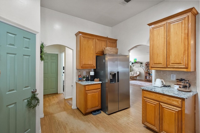 kitchen with backsplash, stainless steel fridge with ice dispenser, light hardwood / wood-style flooring, and light stone countertops