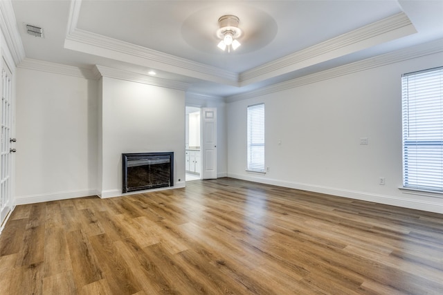 unfurnished living room with a healthy amount of sunlight, a raised ceiling, light hardwood / wood-style floors, and crown molding