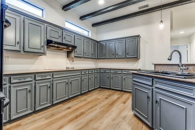 kitchen with black electric stovetop, sink, beam ceiling, decorative light fixtures, and light hardwood / wood-style floors