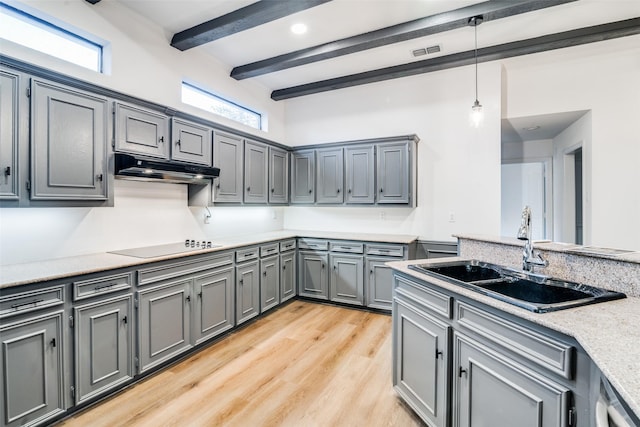 kitchen featuring black electric stovetop, light wood-type flooring, sink, pendant lighting, and beamed ceiling